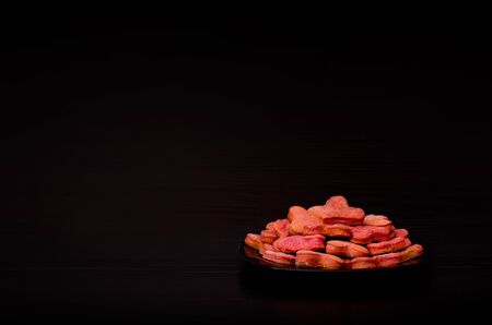 Black plate with red heart-shaped cookies on a black table, Valentine's Day.Side view, copy spaceの写真素材