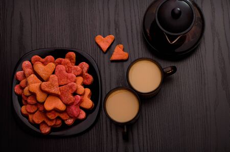 Red heart-shaped cookies, two cups of tea with milk and teapot. Valentine's Dayの写真素材