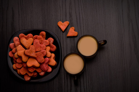 Red heart-shaped cookies and two mugs of coffee with milk on a black table. Valentine's Dayの写真素材