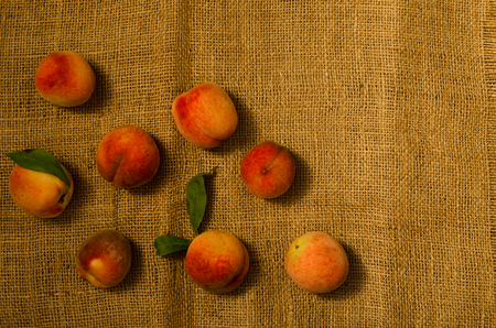 Ripe peaches with leaves on sackcloth, top viewの写真素材