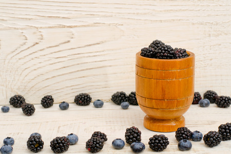 Wooden vessel with blackberries, blueberries and blackberries on the edges, light backgroundの写真素材