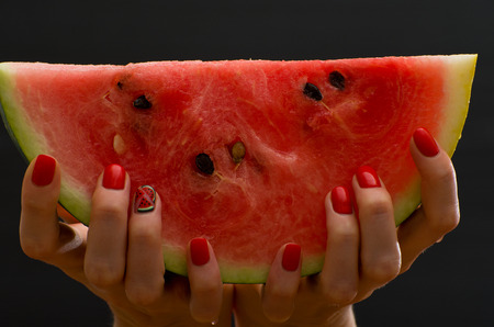 Large slice of ripe watermelon in female hands on a black background, close-upの写真素材