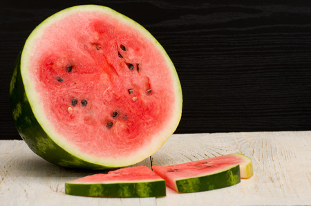 Halves cut watermelon slices on a light wooden table, black backgroundの写真素材