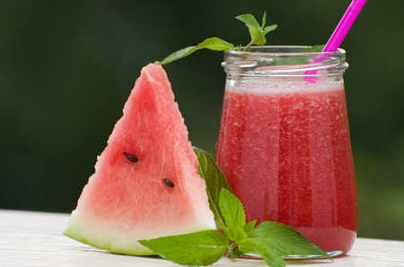 Slice of watermelon, a jar of watermelon smoothie with mint on greenery backgroundの写真素材