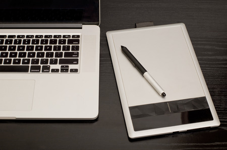 Graphics tablet with a pencil, some laptop on black wooden table, close-upの写真素材