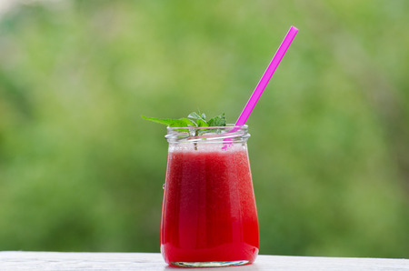 Watermelon smoothie with sprig of mint and a straw on a blurred background of greensの写真素材