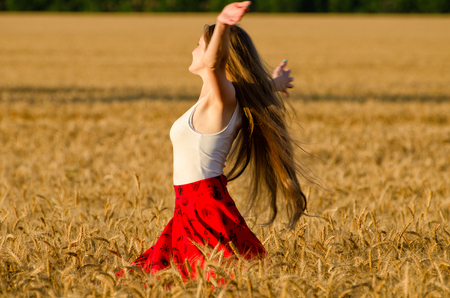 Girl with long hair whirling in a wheat field arms spreadの写真素材