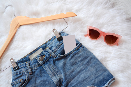 Short denim shorts on trempel with blank business card in a pocket, on white fur and pink glasses. View from aboveの写真素材