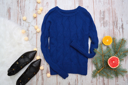 Blue sweater with braids and black shoes on a wooden background. Citrus, fir branch garland....