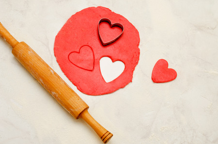 Red dough with a rolling pin and cut out hearts on a white tableの写真素材