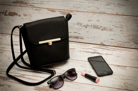 Little black ladies handbag, sunglasses, phone and lipstick on wooden background. fashion conceptの写真素材