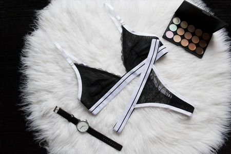 Black sports set lace lingerie on a white fur. Watches, eyeshadow. Fashionable concept, top viewの写真素材