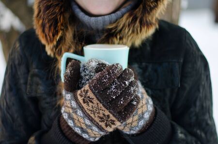 Gloved hands holding a cup of tea outdoors