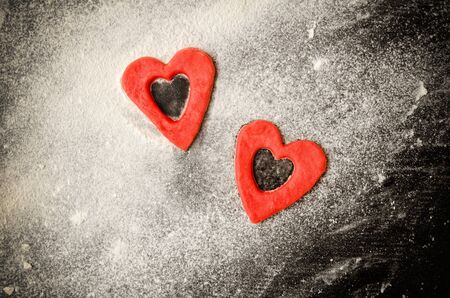 Two red hearts cut out of the dough on the floured table, black table, space for text. top viewの写真素材