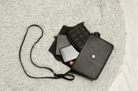 Open black handbag, wallet, mobile phone and lipstick in it. Grey fur background, top view. fashion conceptの写真素材