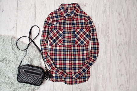 Plaid ladies shirt, black handbag on the artificial fur. Fashionable concept, wooden background, top...