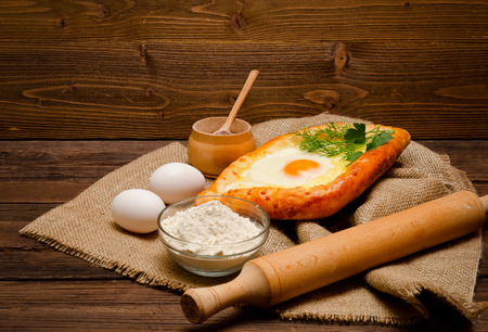 Khachapuri with eggs on sackcloth, salt, flour, eggs and parsley on the wooden table, side view