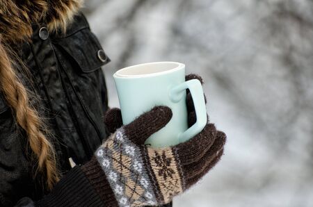 Girl in gloves holding cup of tea, white snowy background