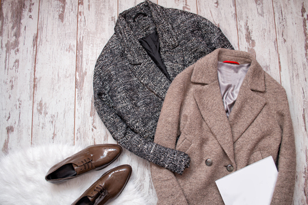 Two woolen coat, brown patent leather shoes on a white fur, white blank sheet, a wooden background. Fashion concept. top viewの写真素材