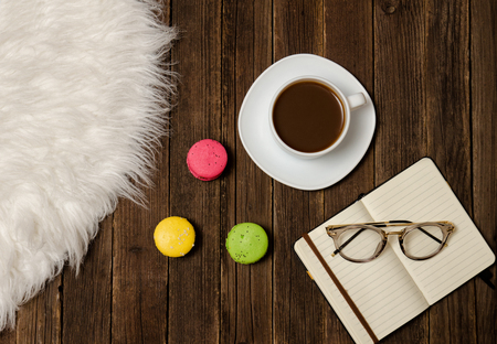 Coffee mug, macarons, notebook and glasses on a wooden table. Top viewの写真素材