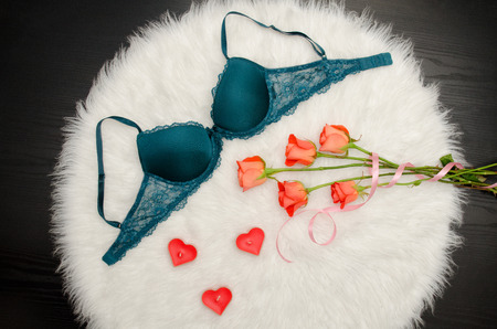 Emerald bra with lace on white fur. Orange roses, heart shaped candles. Fashionable concept. Top viewの写真素材