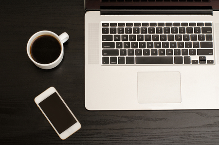 Laptop keyboard, phone and coffee mug on a black table, close-upの写真素材