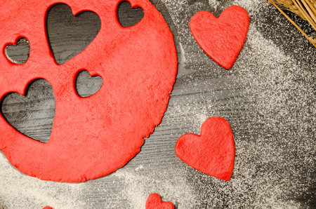 Red dough with cut-out hearts and flour on the black table. top viewの写真素材