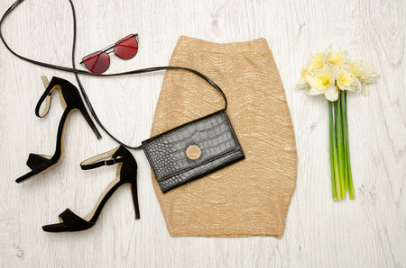 Golden skirt, shoes, clutch, glasses and a bouquet of daffodils. Fashionable concept. Wooden background.の写真素材