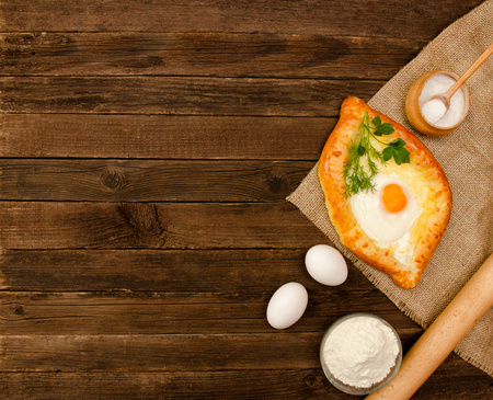 Khachapuri with eggs on sackcloth, salt, flour and eggs on the wooden table, copy spaceの写真素材