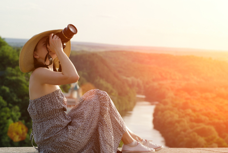 Girl sits and takes pictures against the background of forest and meandering riverの写真素材