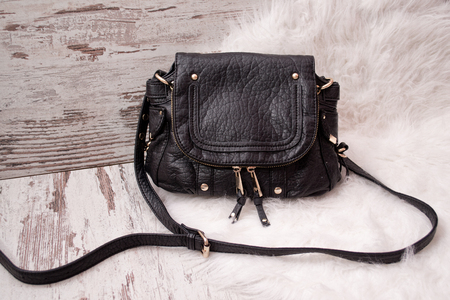 Black bag with locks on a wooden background, white faux fur. Fashionable conceptの写真素材