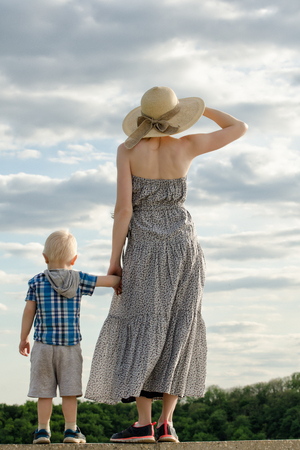 Mom and son stand on a hill and look into the distance against the sky, the view from the backの写真素材