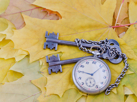Ancient keys and a pocket watch lie on yellow maple autumn leaves