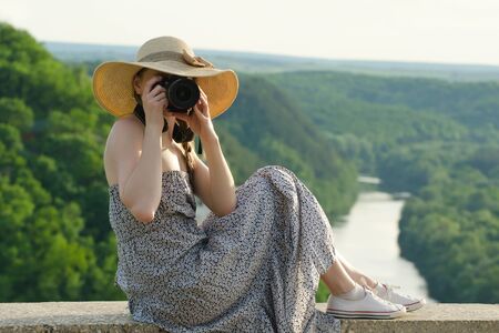 Girl in hat takes pictures against the background of green forest and riverの写真素材