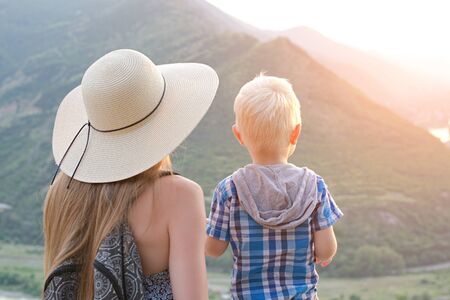 Mom and son stand with their backs against the background of the green mountainsの写真素材
