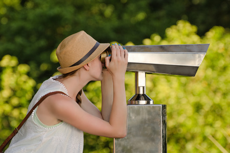 Girl in hat looks into big binoculars. Park in the backgroundの写真素材