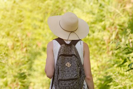 Girl in a hat and a backpack stands in a park. Back viewの写真素材