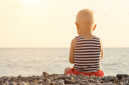 Boy in striped t-shirt sitting on the beach. Back viewの写真素材