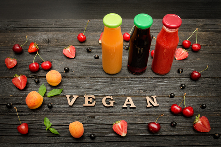 Three bottles with juice, fruit and inscription vegan on a dark wooden background, food conceptの写真素材