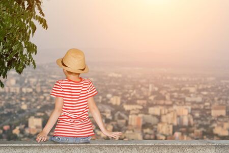 Boy sitting and looking at the city from a height. Rear view, evening timeの写真素材