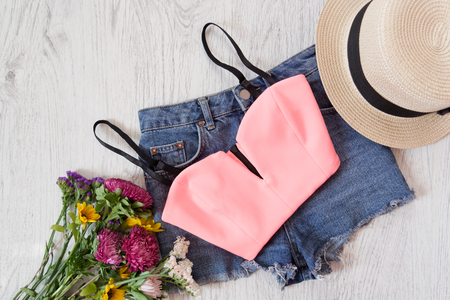 Pink top, denim shorts, hat and bouquet of wildflowers. Fashionable conceptの写真素材