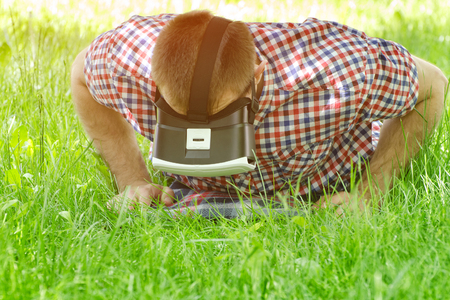 Man in a helmet of virtual reality lies on a green grass and looking downの写真素材