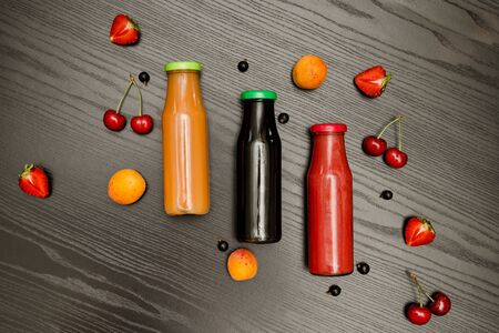 Three bottles with juice, fruits on a black wooden background, food conceptの写真素材