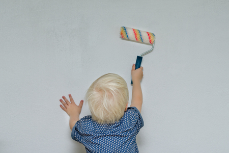 Small blond boy paints a wall with a roller. View from the back
の写真素材