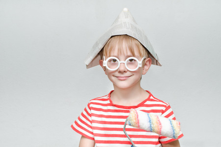 Boy in a paper hat is playing in a painter. Portrait. Roller for paintingの写真素材
