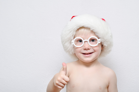 Little blond boy wearing Santa's hat and glasses. Thumb upの写真素材