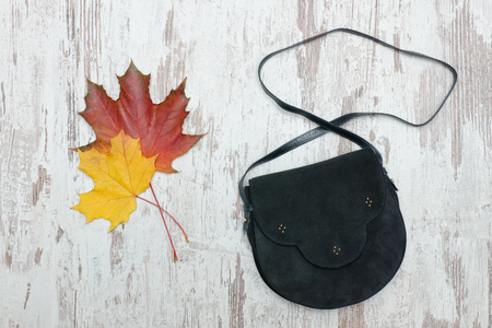 Black handbag on a wooden background and maple leaves. Fashionable concept.の写真素材