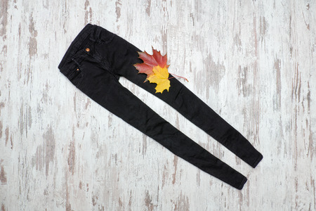 Black jeans on a wooden background and maple leaves. Fashionable concept.の写真素材