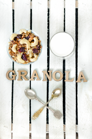 Glass of yogurt and a bowl with granola on a white wooden box. Inscription Granola wooden lettersの写真素材