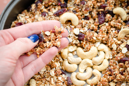 Female hand holds granola against the background of baking sheet with granola. Close-upの写真素材